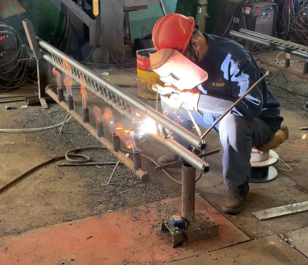 Welder performing manual welding on T91 steel tubes with continuous flame heating to maintain critical preheat temperature.